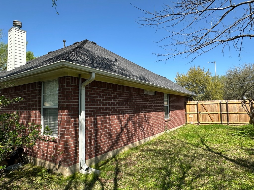 Side view of a single-story brick house with a sloped roof, showcasing exterior maintenance aspects like siding and gutters, under a clear blue sky.